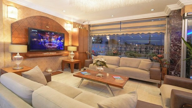 A modern living room with a large flat-screen TV, comfortable sofas, a coffee table, and a view of the cityscape through large windows. - Hotel Akyildiz (Istanbul)