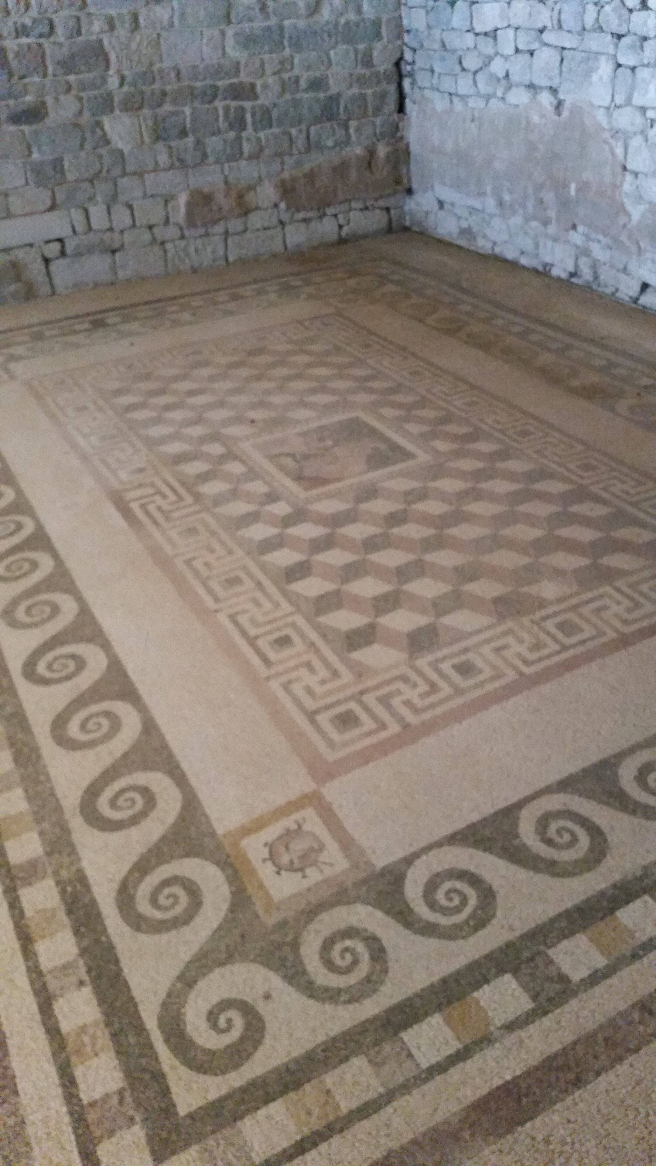 Una habitación con alfombra estampada, paredes de piedra y suelo de baldosas.