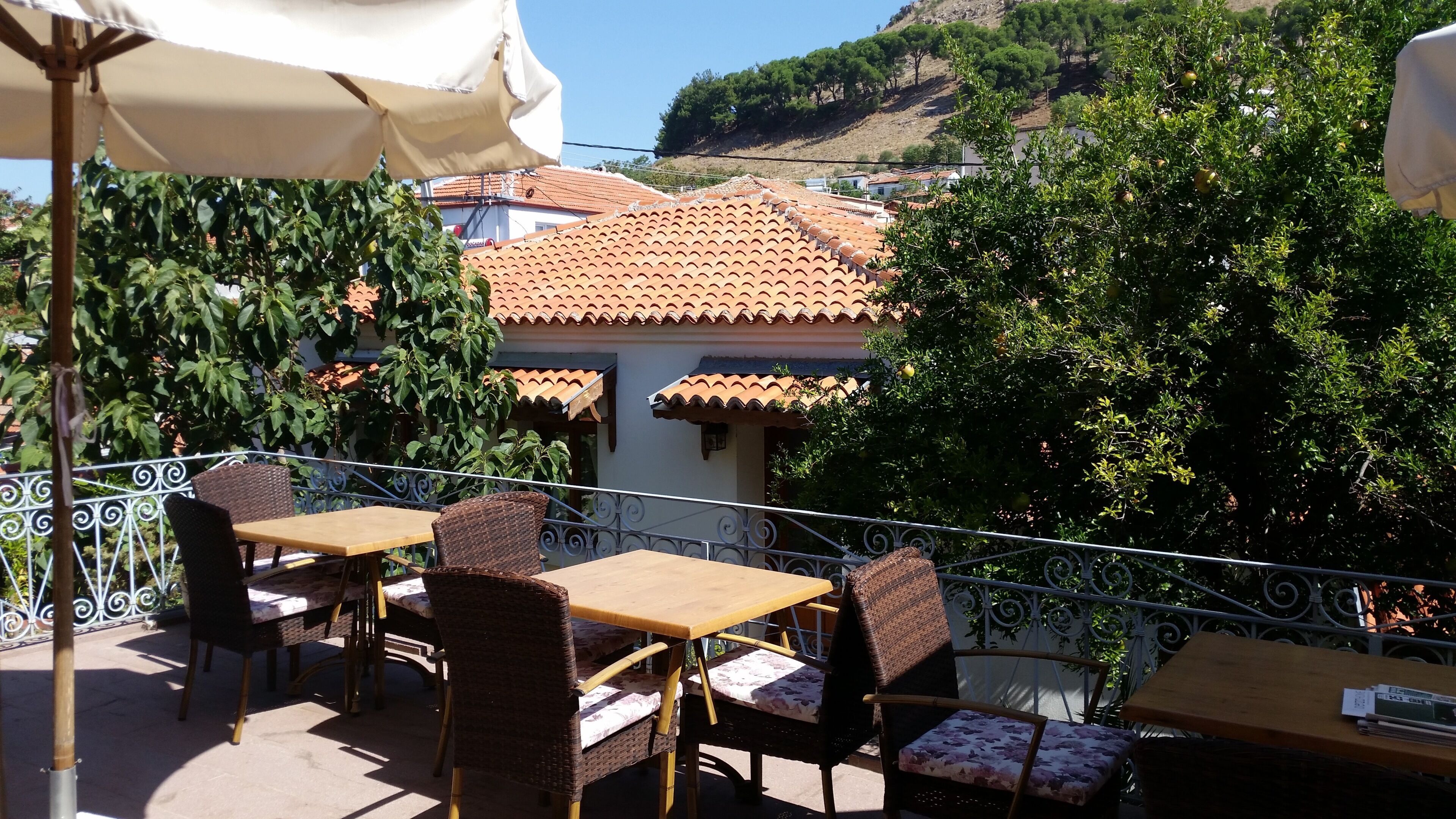 An outdoor patio with tables and chairs, a white umbrella, and a view of a hillside with buildings.