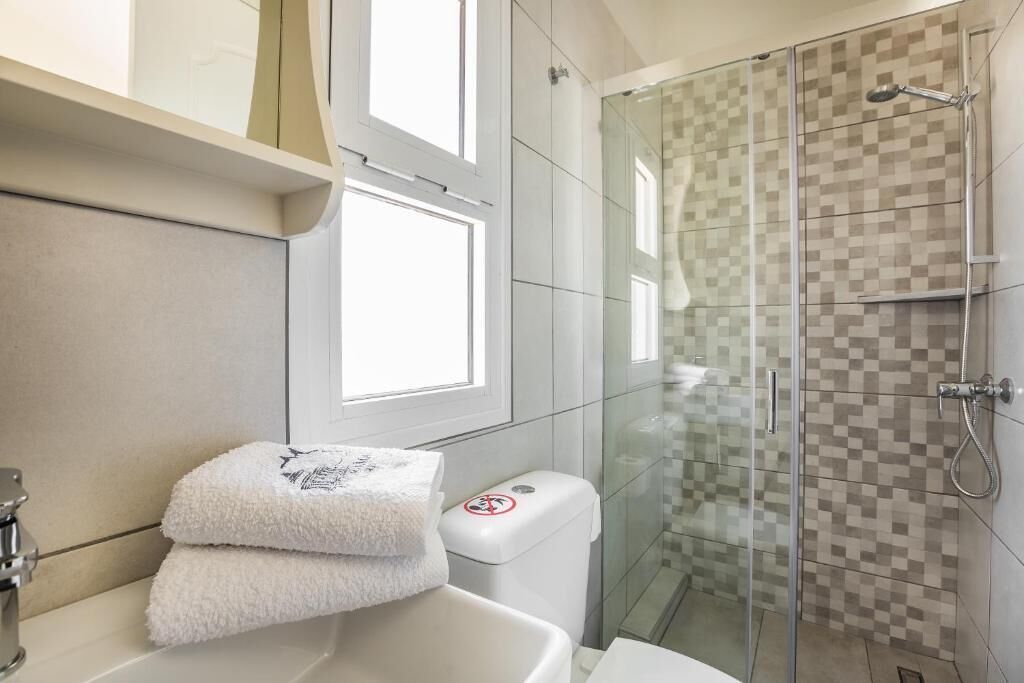 Un baño moderno con cabina de ducha de vidrio, un lavamanos blanco y un ventanal que proporciona luz natural.