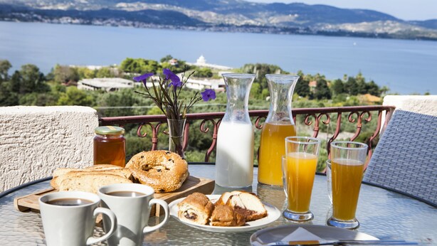 Une table de petit-déjeuner avec des croissants, du café et du jus de fruits, donnant sur un magnifique lac et des montagnes.