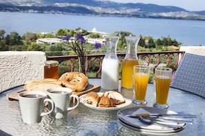A breakfast table with croissants, coffee, and juice, overlooking a scenic lake and mountains.