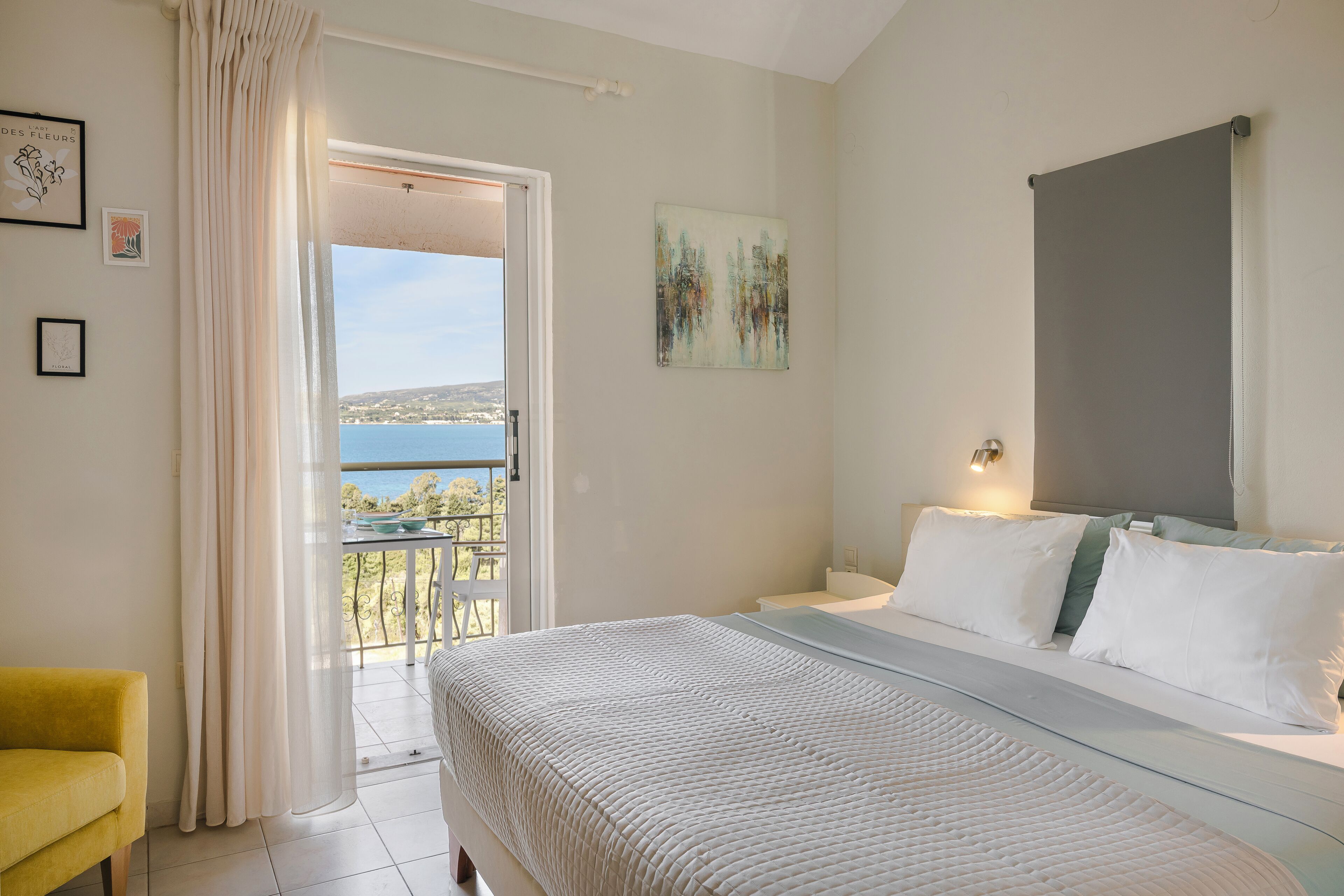 Quarto com cama, uma cadeira amarela, varanda com vista e um quadro na parede.