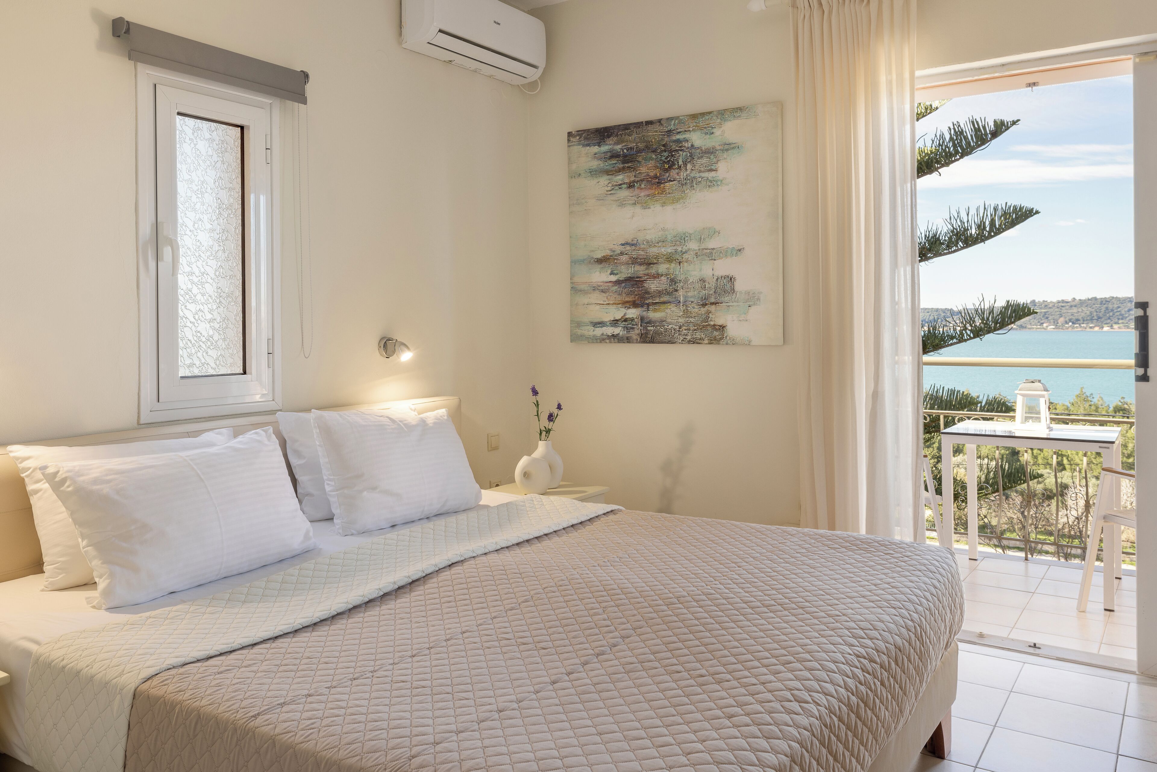 A bedroom with a bed, a window, a painting, and a balcony with a view.