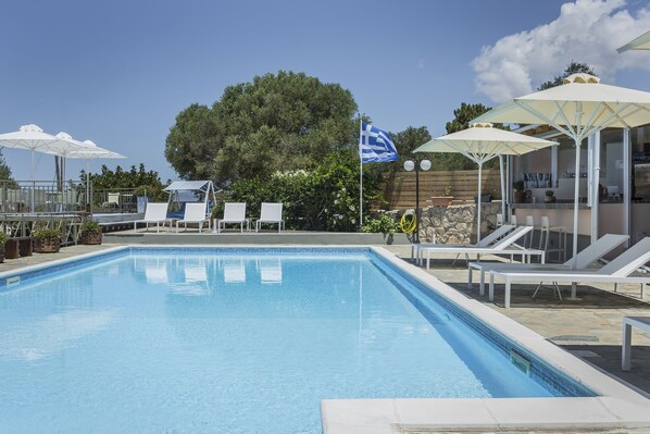 A swimming pool with lounge chairs and umbrellas, surrounded by a wooden fence and greenery.