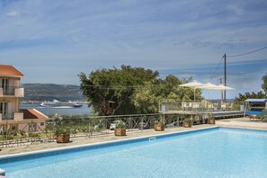 A swimming pool with a view of the sea, a covered seating area, and a building with a red roof. - Panorama Fanari Studios & Apartments (Kefalonia)