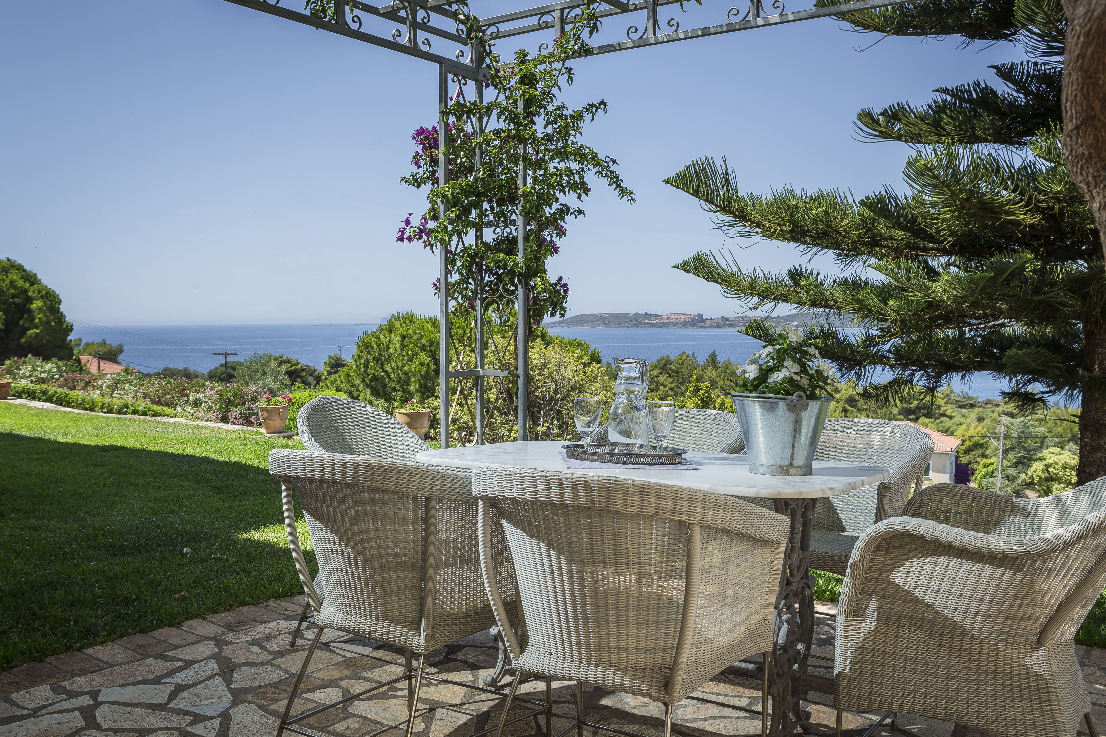 An outdoor patio with wicker furniture, a metal table, and a view of the sea.
