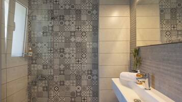 A bathroom with patterned tiles, a white sink, a mirror, and a shower area.