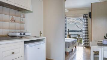 Cocina pequeña con estufa, refrigerador y zona de comedor. Se ve un balcón con cortina a cuadros y vista al mar.