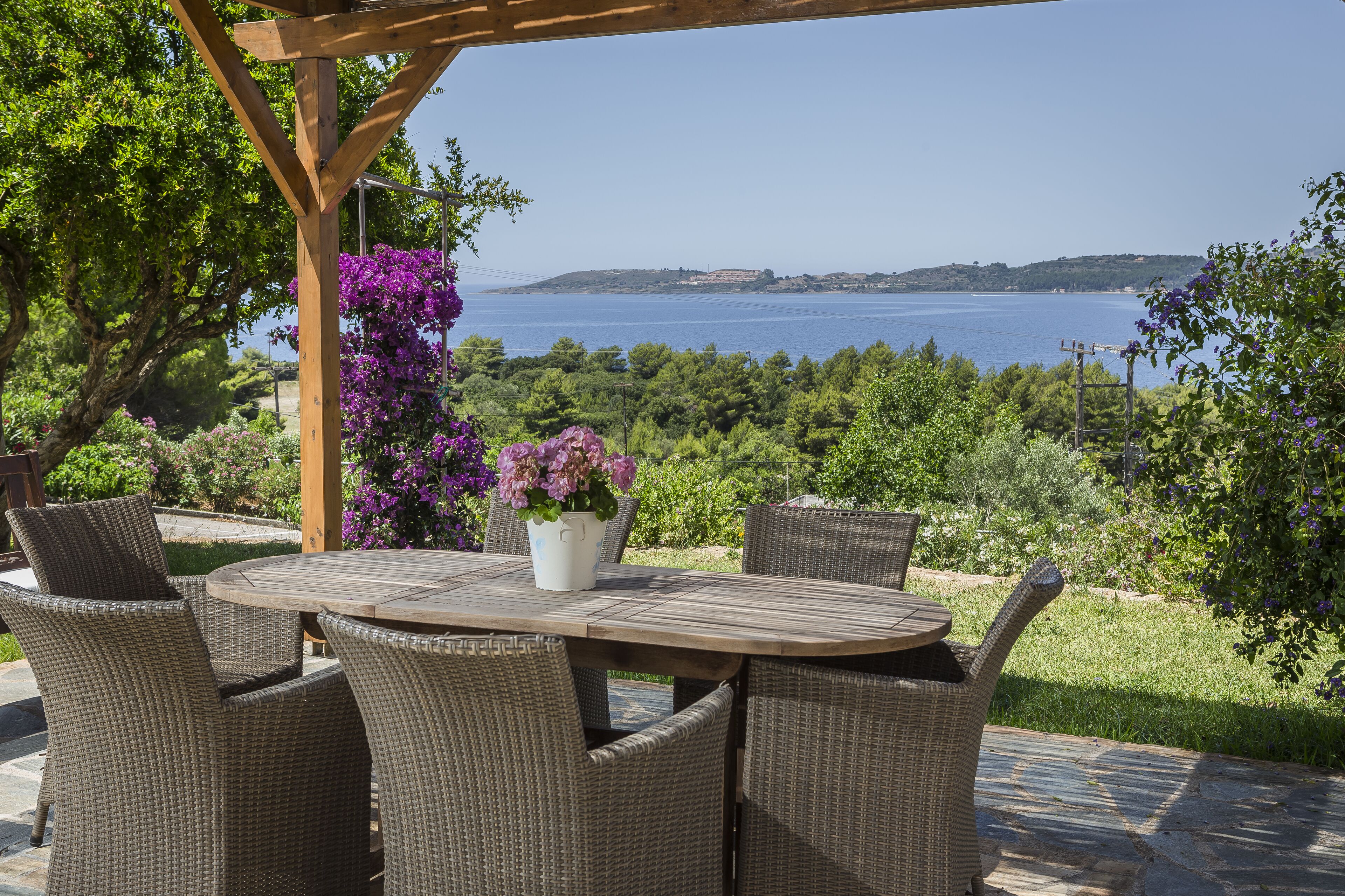Ein Essbereich im Freien mit Korbstühlen und einem Tisch, mit Blick auf eine malerische Aussicht auf das Meer und die Hügel.
