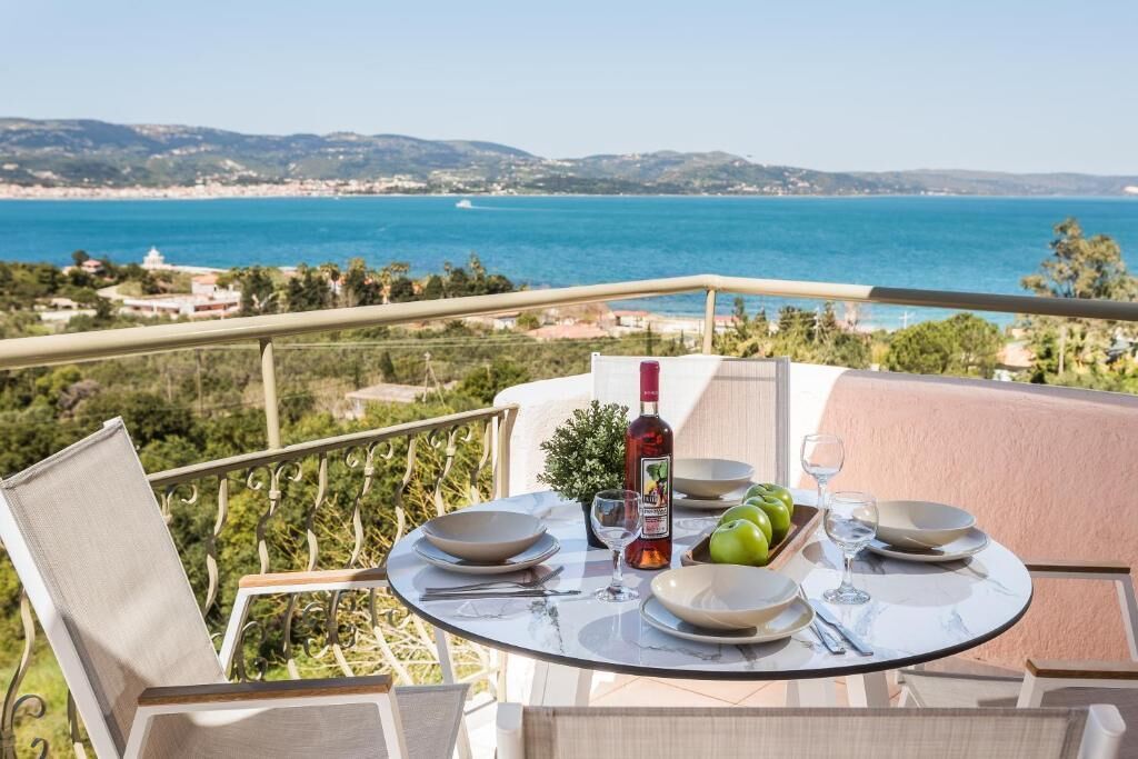 Una mesa en un balcón con vistas al mar, una botella de vino y manzanas verdes.