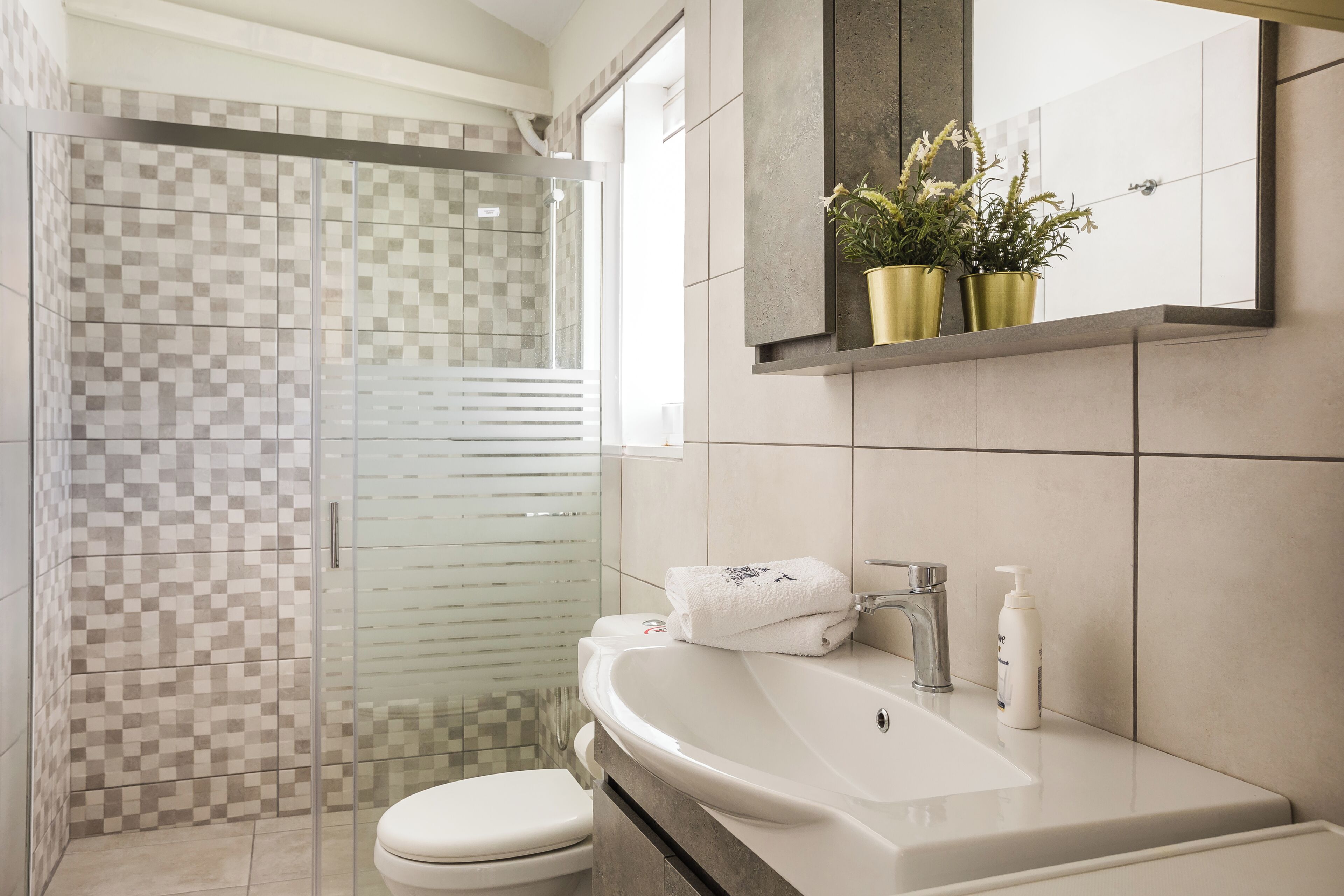 A bathroom with a glass shower enclosure, a white sink, and a mirror above it.