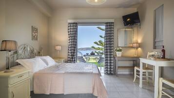 A bedroom with a bed, bedside table, lamp, and a view of the sea.