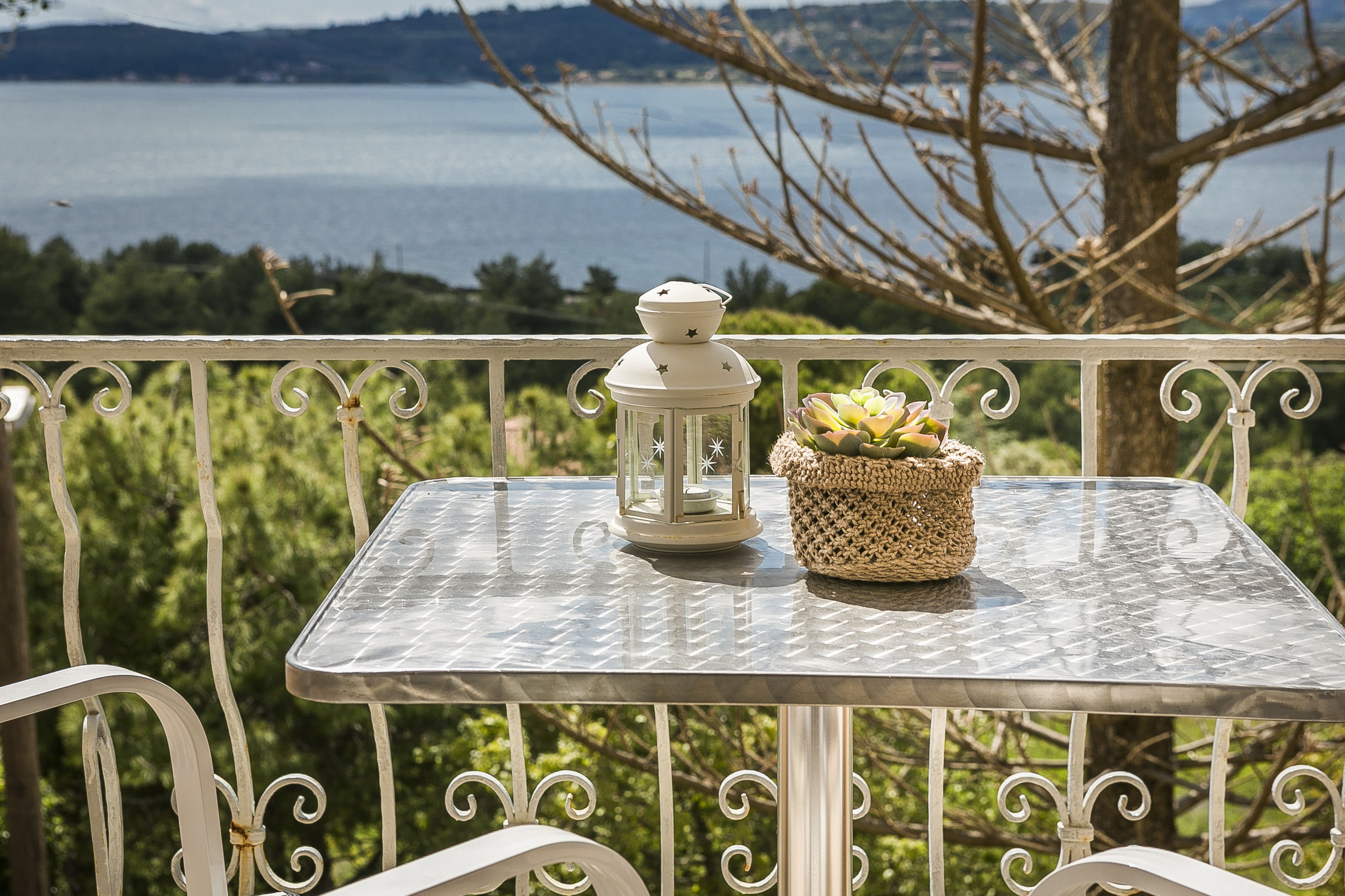A balcony with a metal table, a white lantern, and a woven basket with succulents.