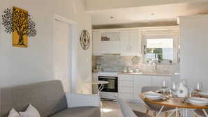 Une cuisine moderne avec des meubles blancs, une table à manger pour quatre personnes et un canapé gris dans l’espace salon.