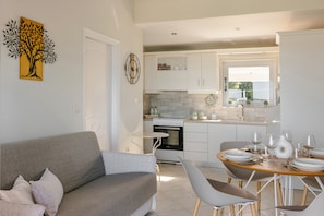 A modern kitchen with white cabinets, a dining table set for four, and a gray sofa in the living area.