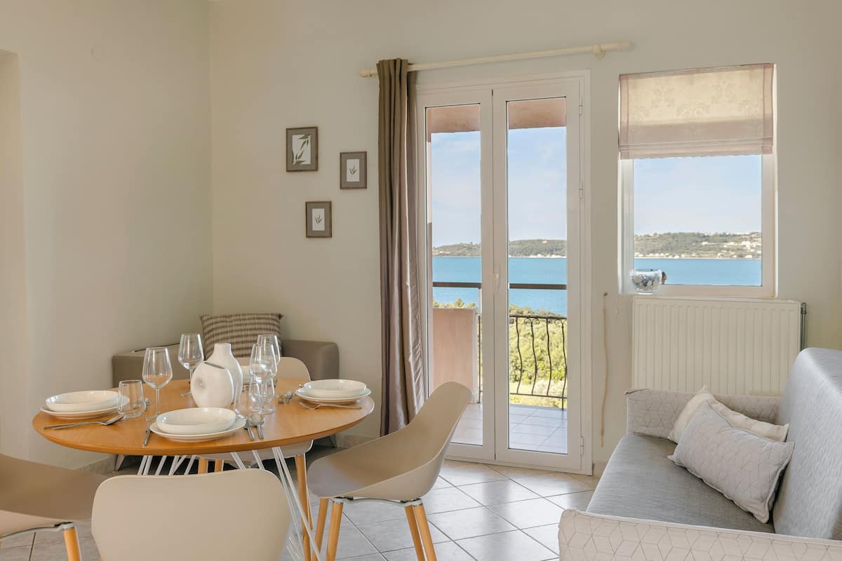 Een eethoek met een tafel voor vier personen, een bank en uitzicht op zee door een schuifdeur.