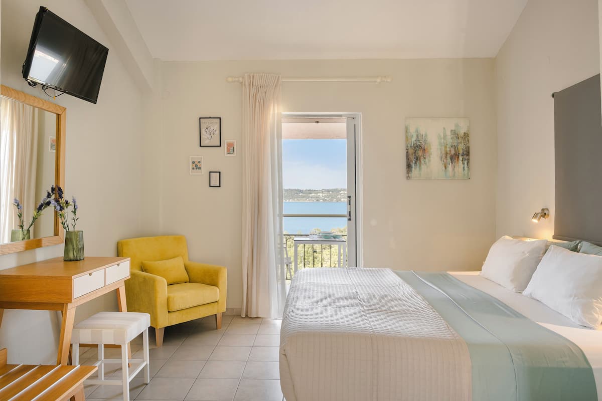 Een slaapkamer met een bed, een bureau, een stoel, een televisie en een balkon met uitzicht.
