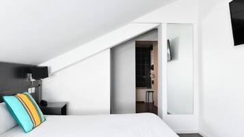Una moderna camera d'albergo con un letto, un comodino, una TV a parete e un bagno visibile attraverso una porta aperta.