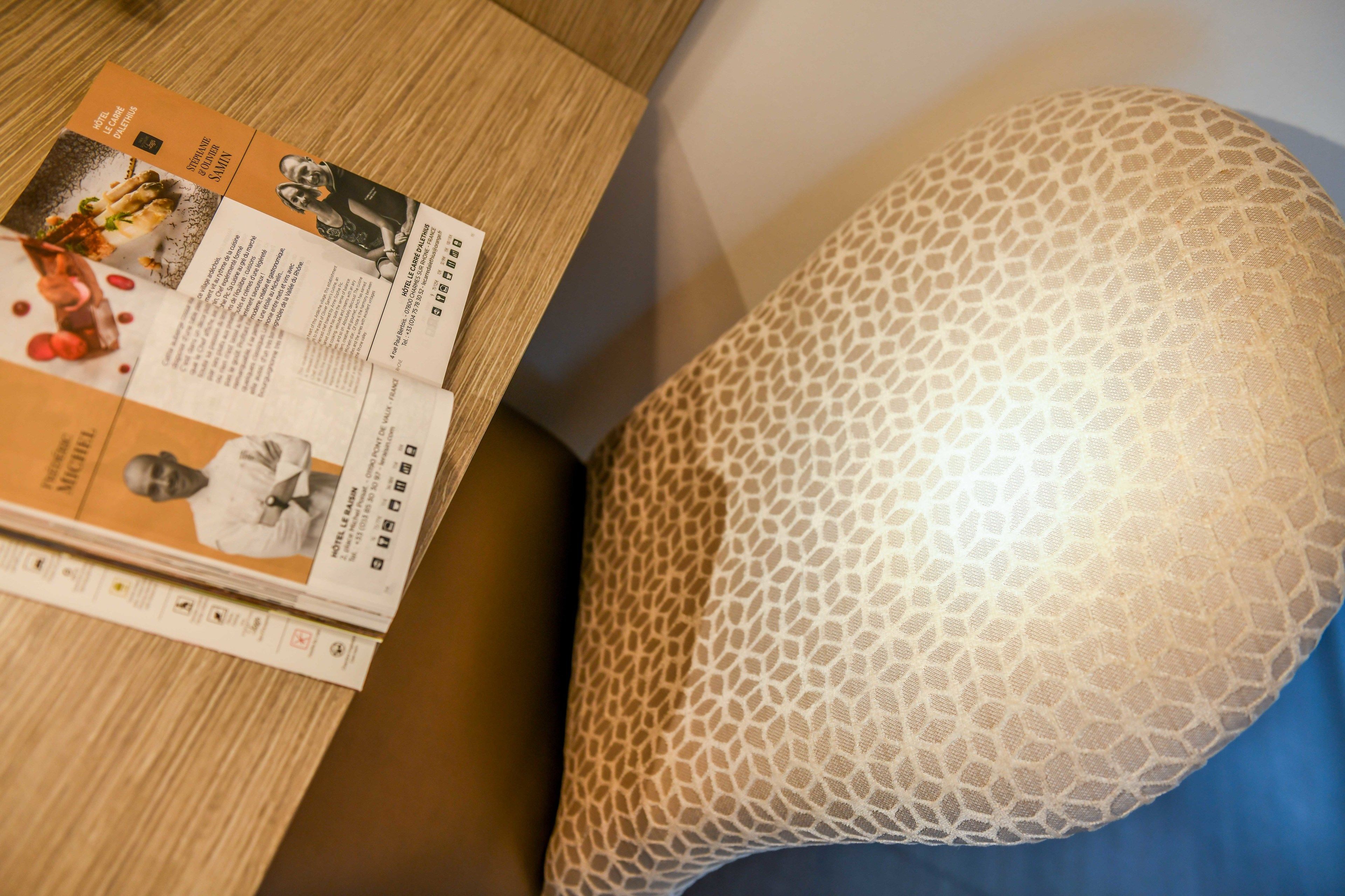 A brochure on a wooden table next to a uniquely patterned pillow.