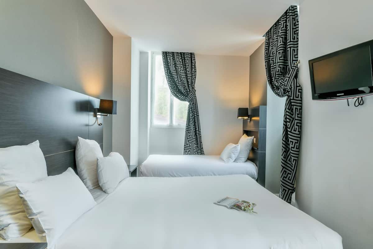 A hotel room with two beds, a flat-screen TV, and patterned curtains.