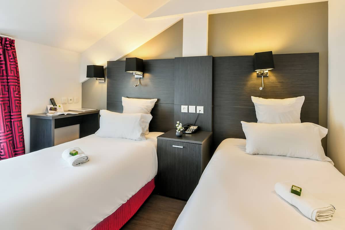 A hotel room with two beds, a desk, and bedside tables with lamps.