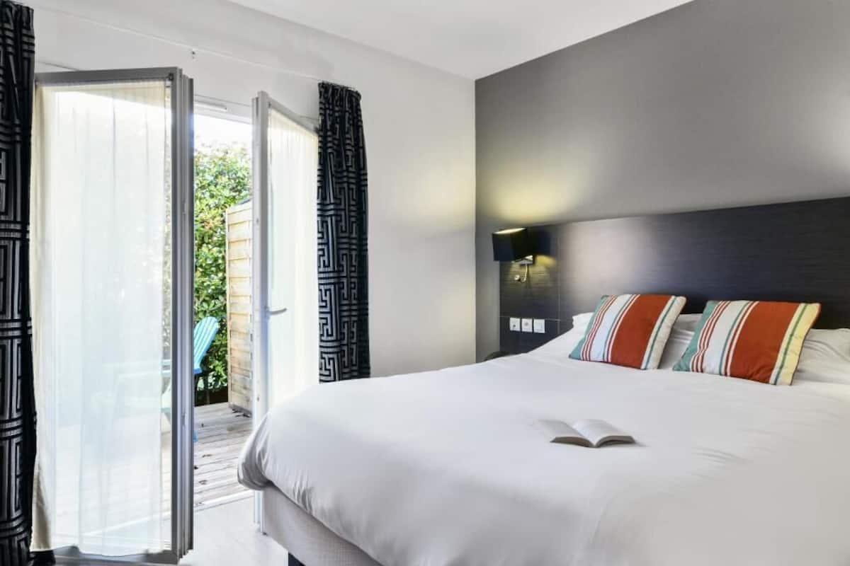 A modern hotel room with a large bed, a bedside table, and a wall-mounted lamp.