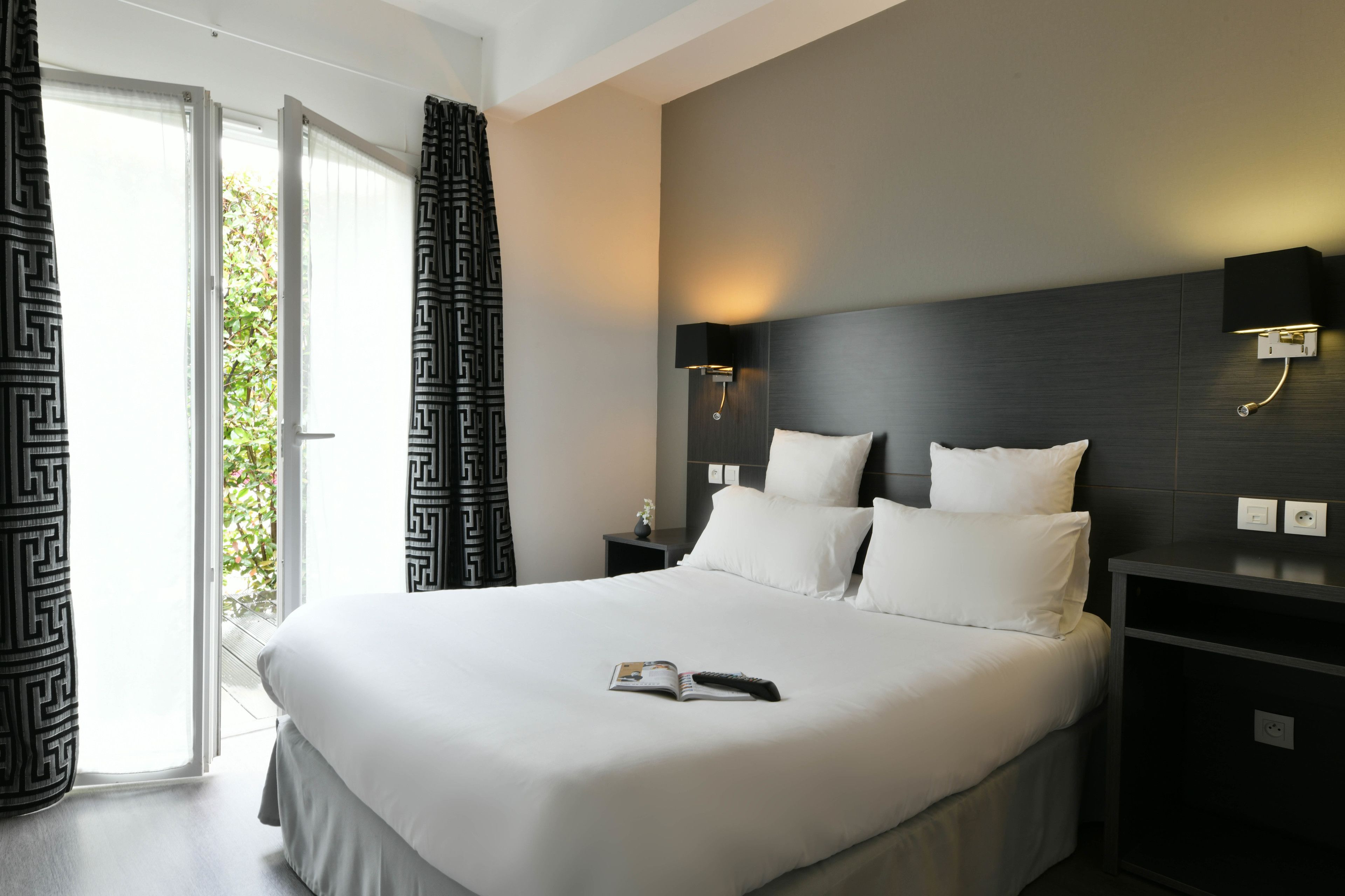 Habitación de hotel con una cama grande, una mesita de noche con lámpara y vistas al exterior a través de una puerta corredera.