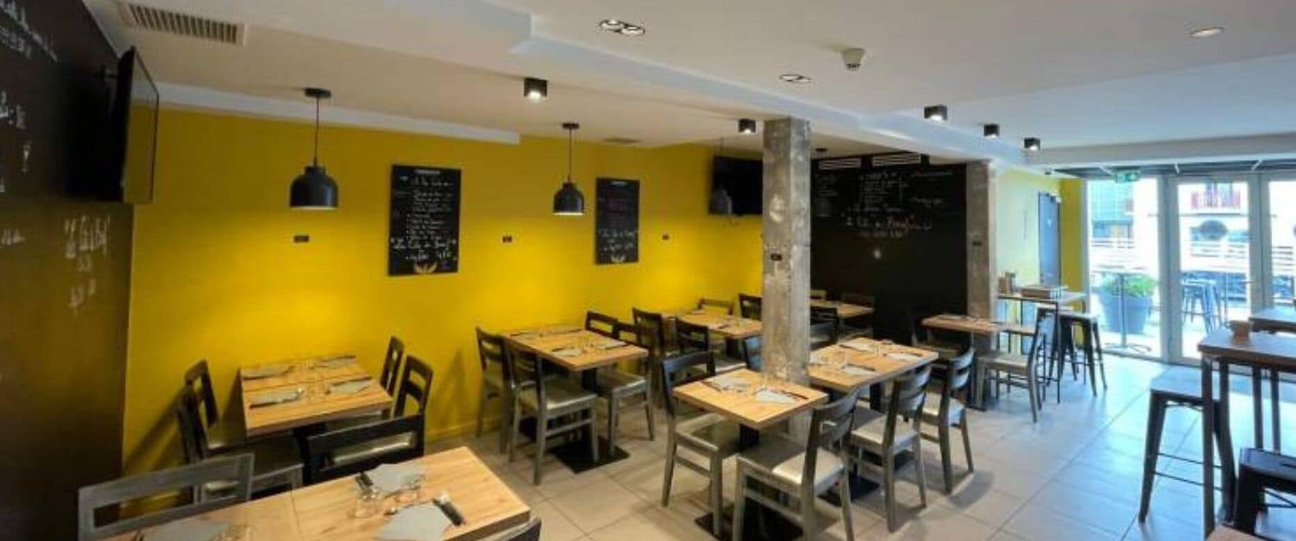 Un restaurante con paredes amarillas, mesas de madera y pizarras con escritura.