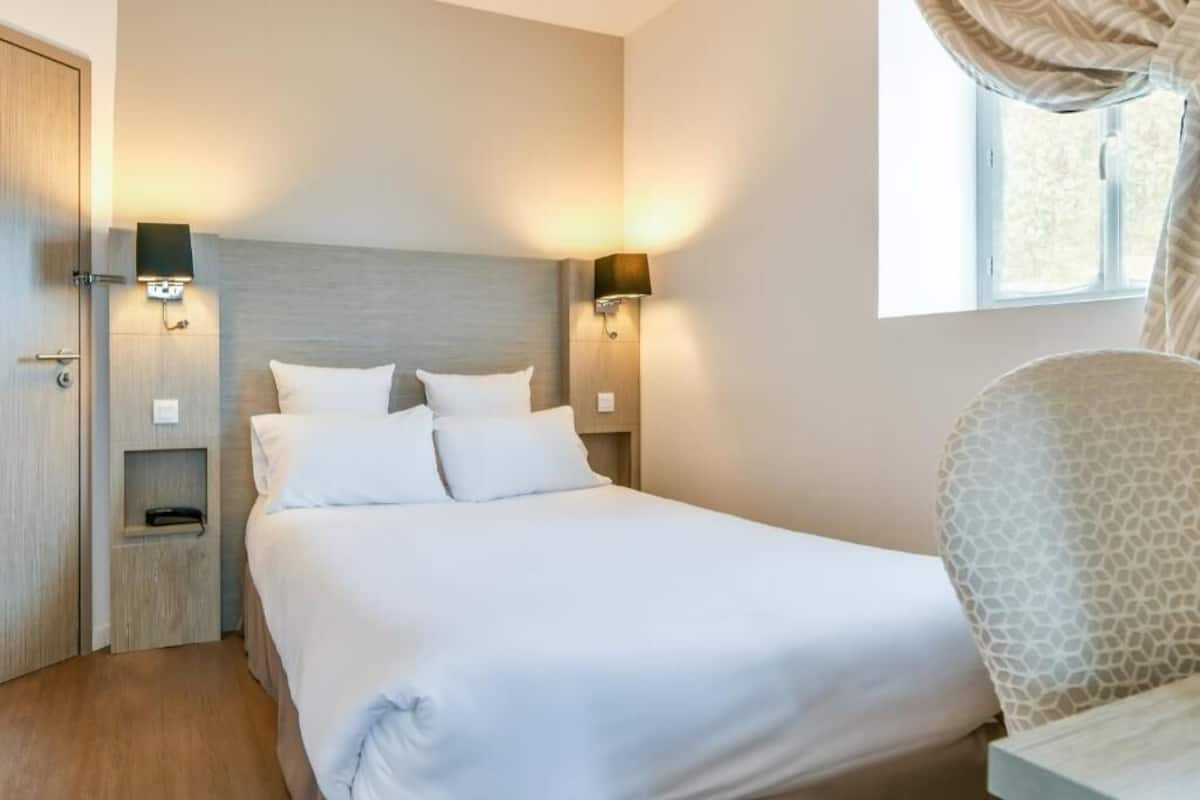 A neatly made bed with white bedding, two bedside lamps, and a nightstand with a lamp.