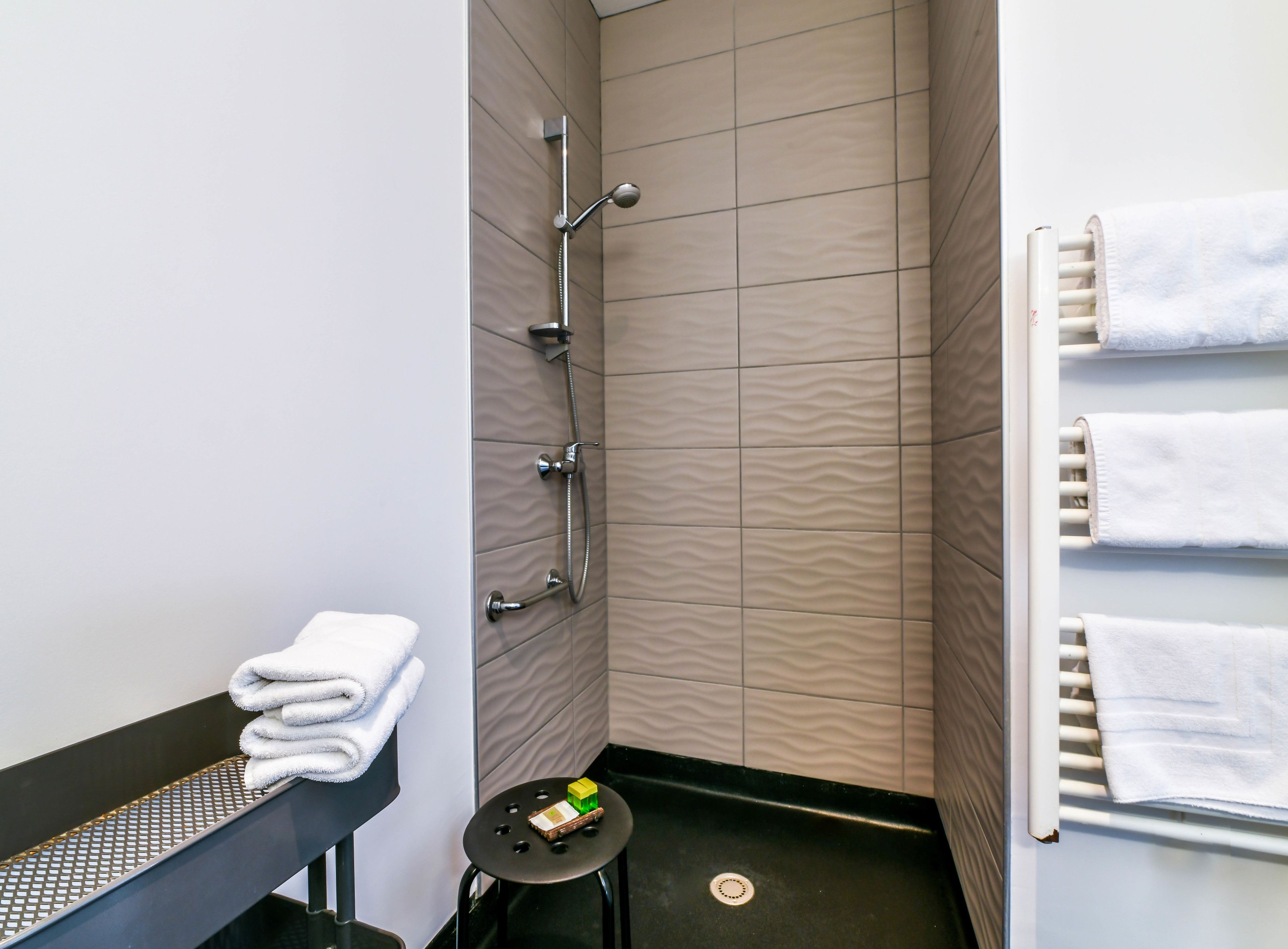 A modern bathroom with a shower, a towel rack with multiple towels, and a small table with a Rubik's cube.
