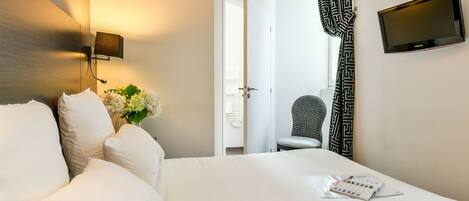 A hotel room with a bed, a wall-mounted TV, a chair, and a door leading to another room.
