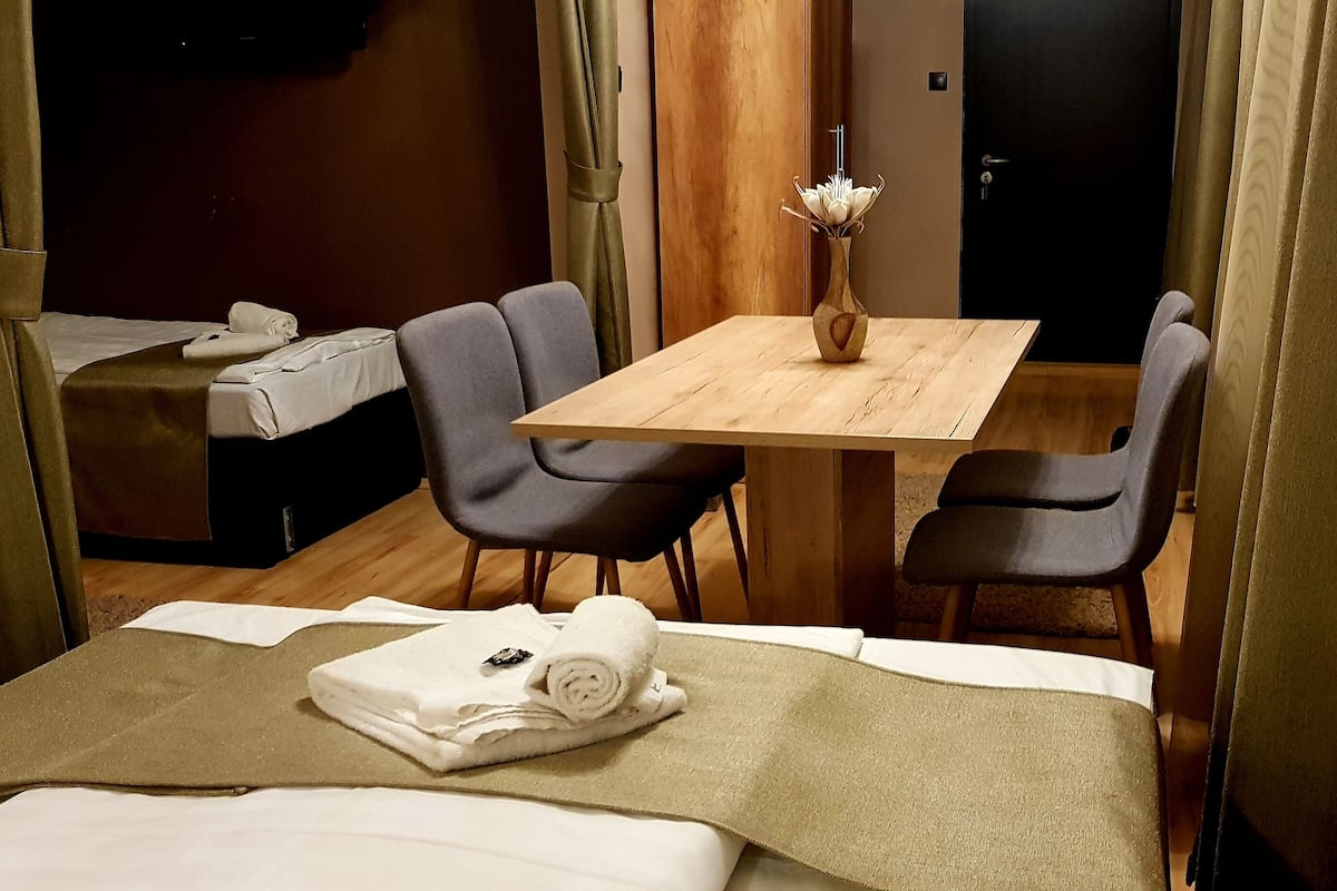 Ein Hotelzimmer mit einem Bett, einem Holztisch, zwei Stühlen, einem kleinen Tisch mit einer Vase und einer Tür.