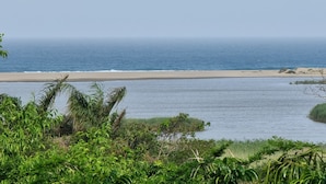 Een kustlandschap met een strand, kalm water en weelderige begroeiing.