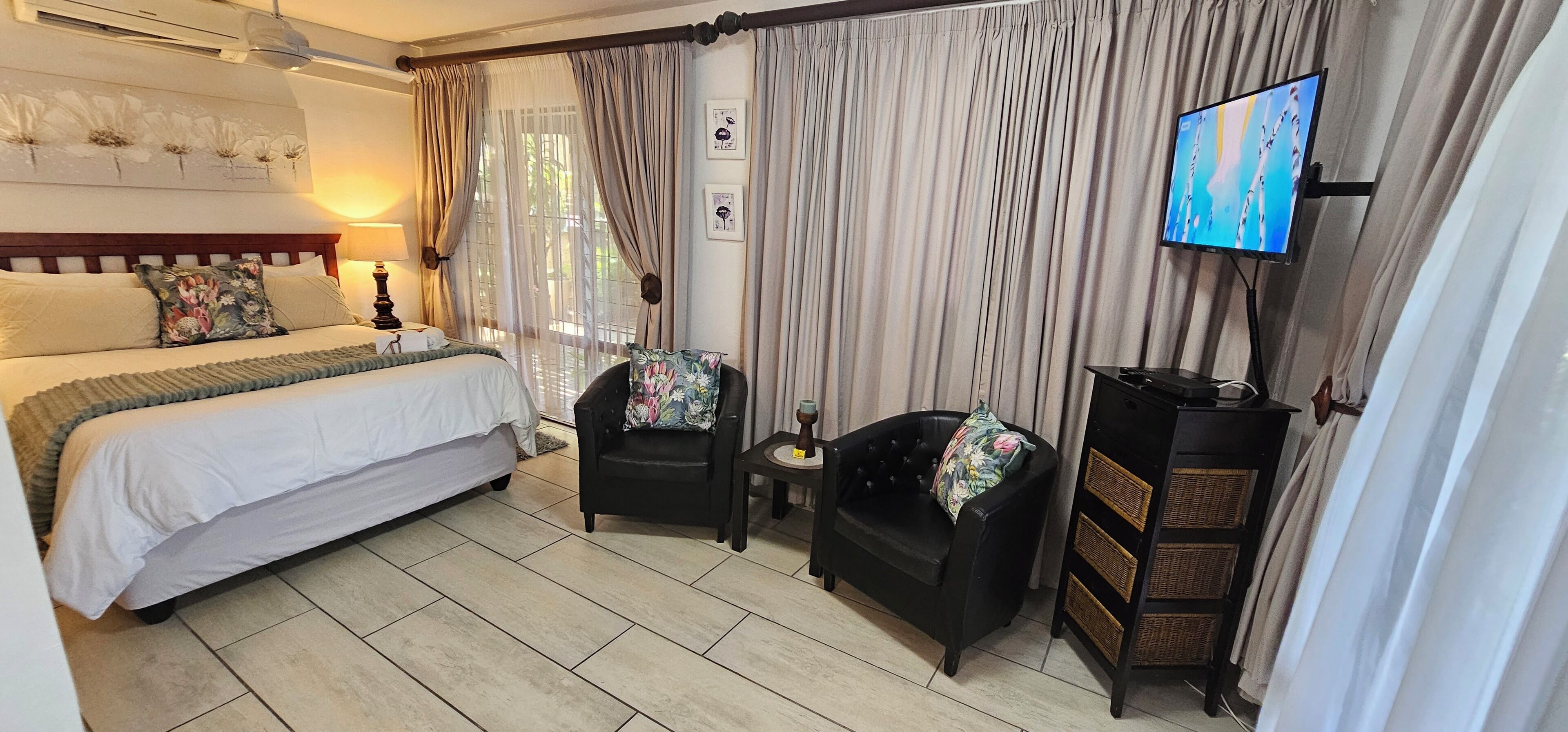Une chambre d’hôtel avec un grand lit, deux fauteuils, une télévision et une petite table.