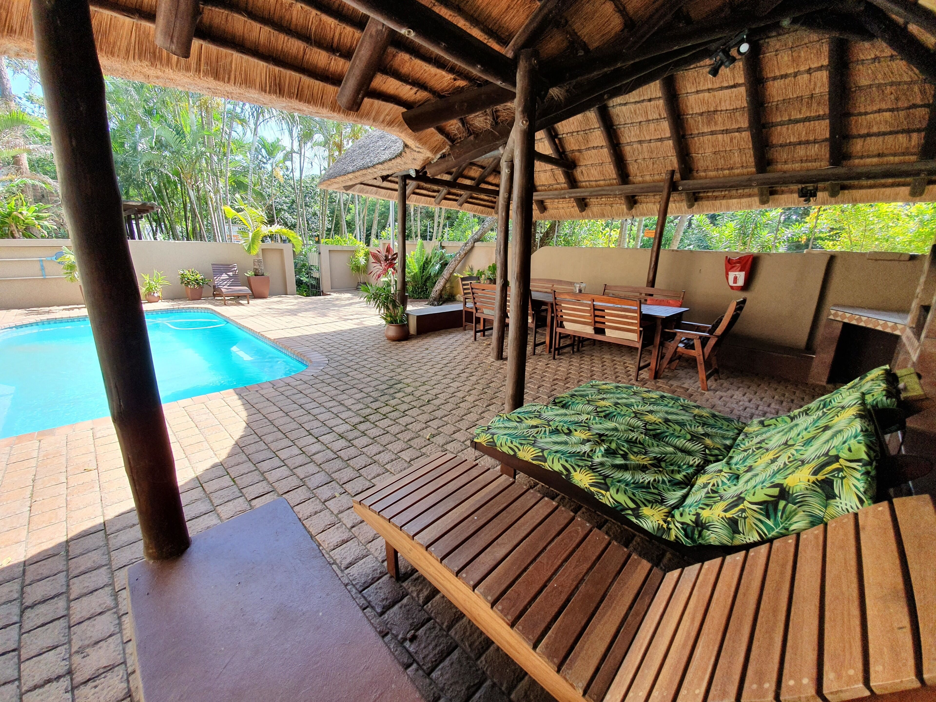 Un espacio al aire libre techado con piscina, muebles de madera y plantas en macetas.