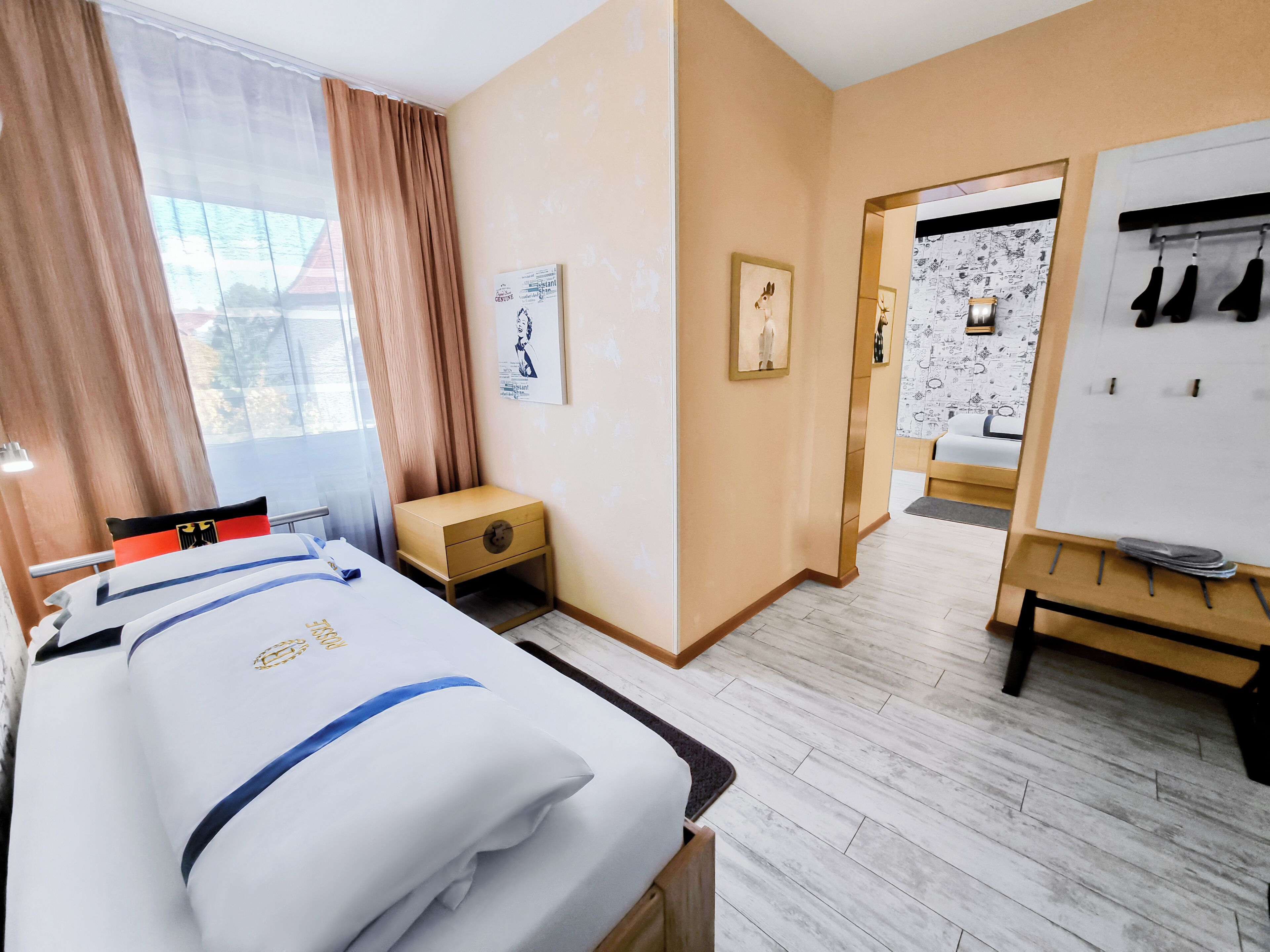 A hotel room with a bed, a small wooden nightstand, a whiteboard, and a coat rack.