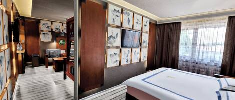 A hotel room with a large bed, a desk with a computer, and a seating area with a sofa and chairs.