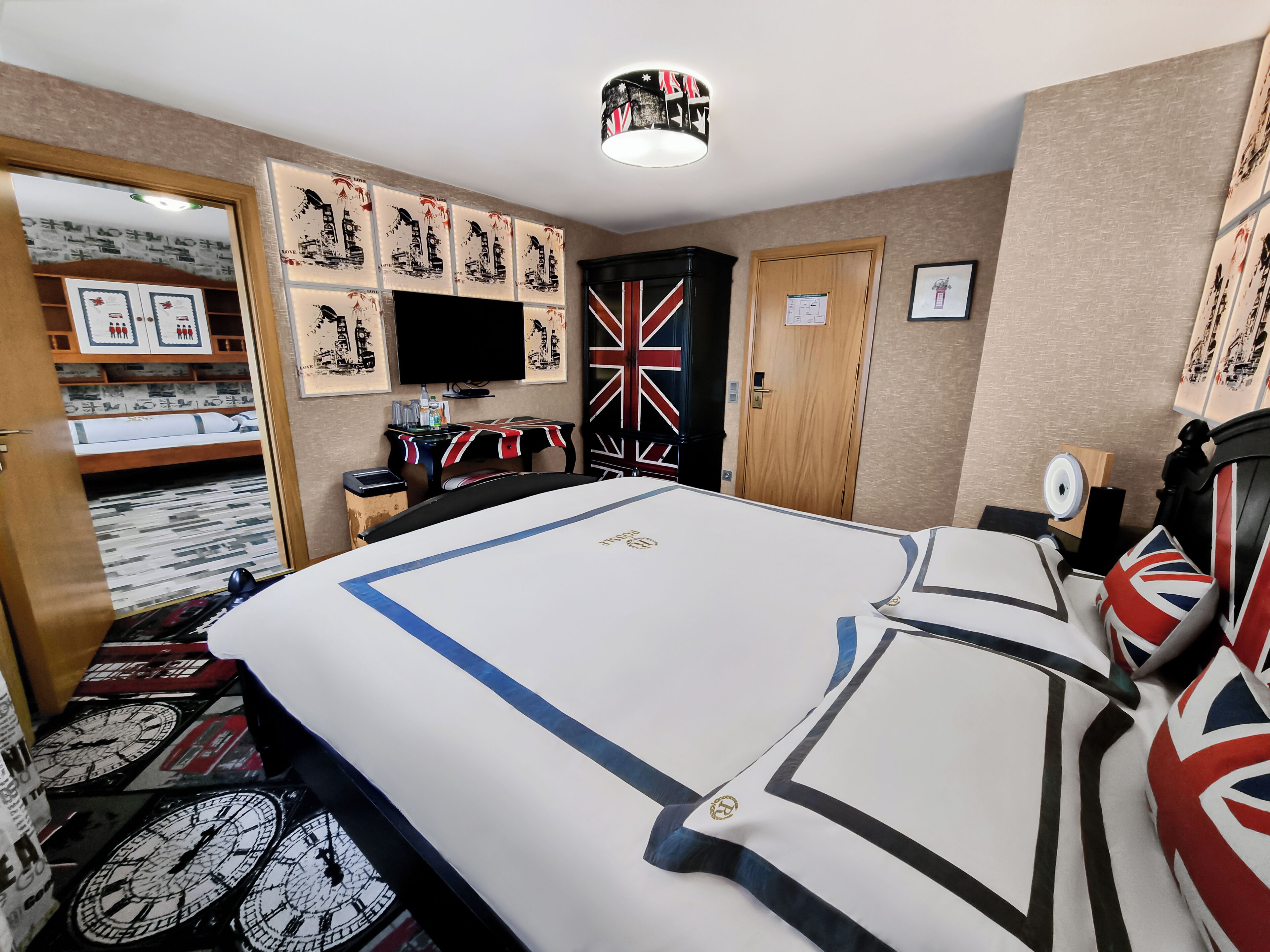 Ein Hotelzimmer mit einem großen Bett, einem Flachbildfernseher, einem Tisch mit Union-Jack-Tischdecke und einer Wand mit gerahmten Kunstwerken.