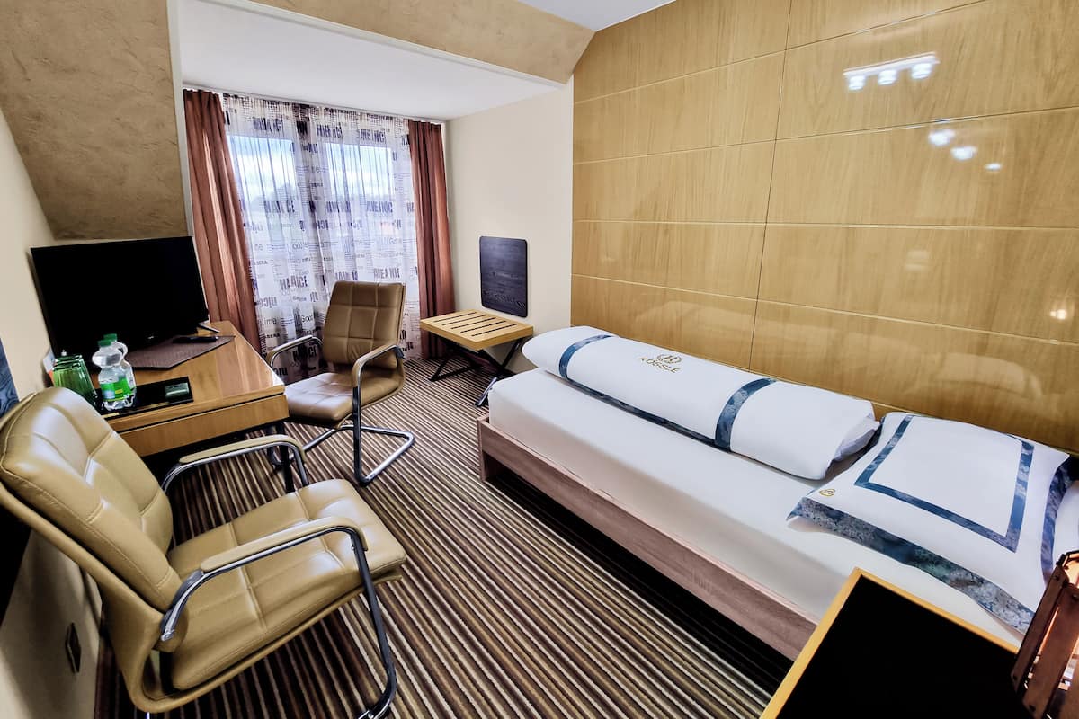 Habitación de hotel con cama, escritorio con computadora, silla, televisor y ventana con cortinas.