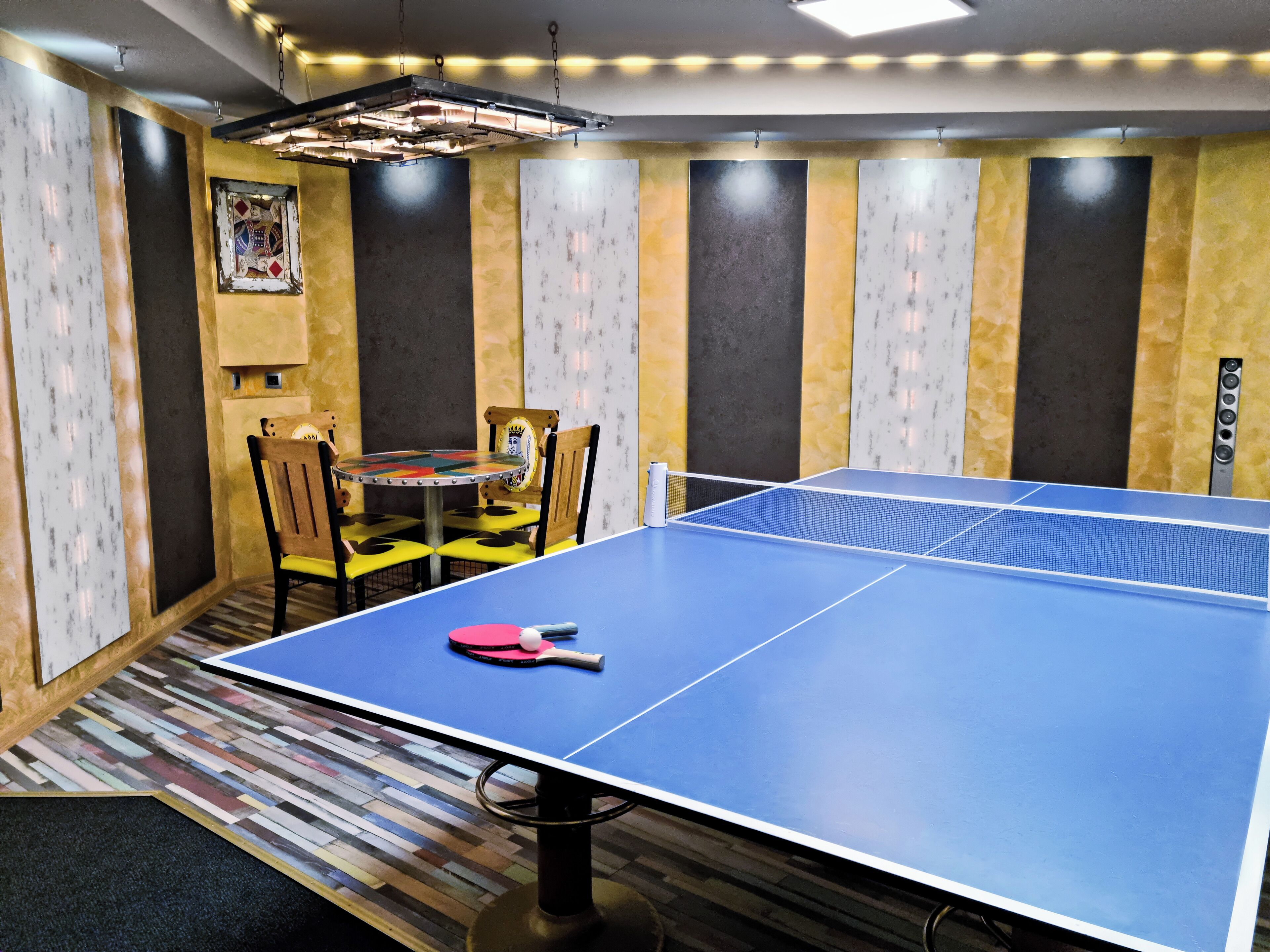 A ping pong table with a net, chairs, and a table with a decorative design.