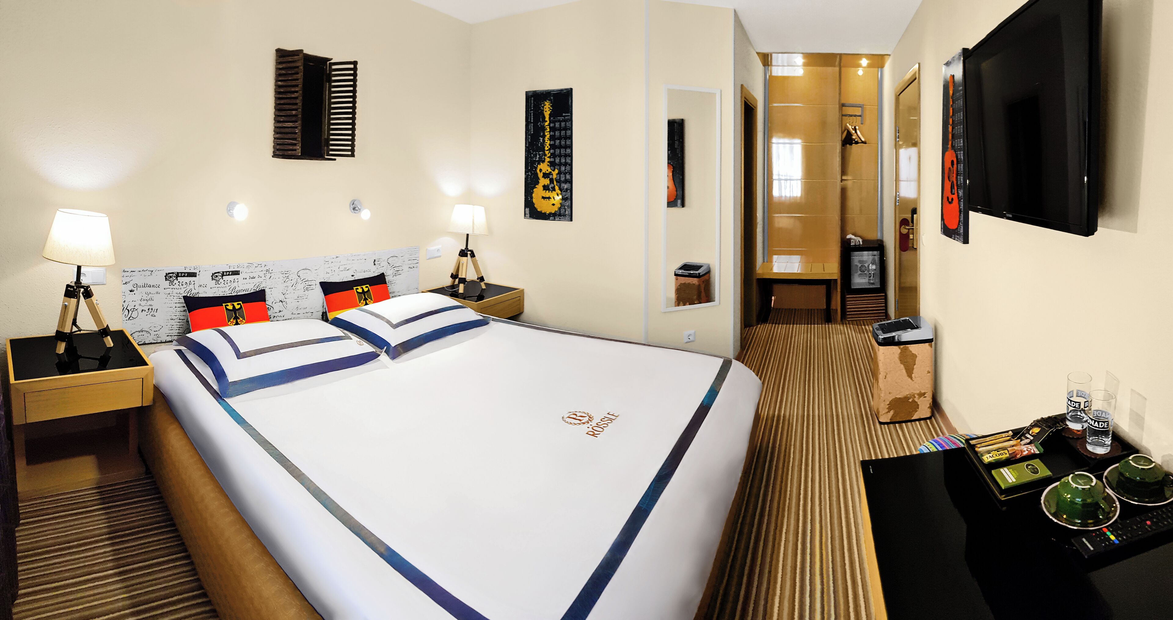 A hotel room with a large bed, bedside tables, a TV, and a bathroom visible through an open door.
