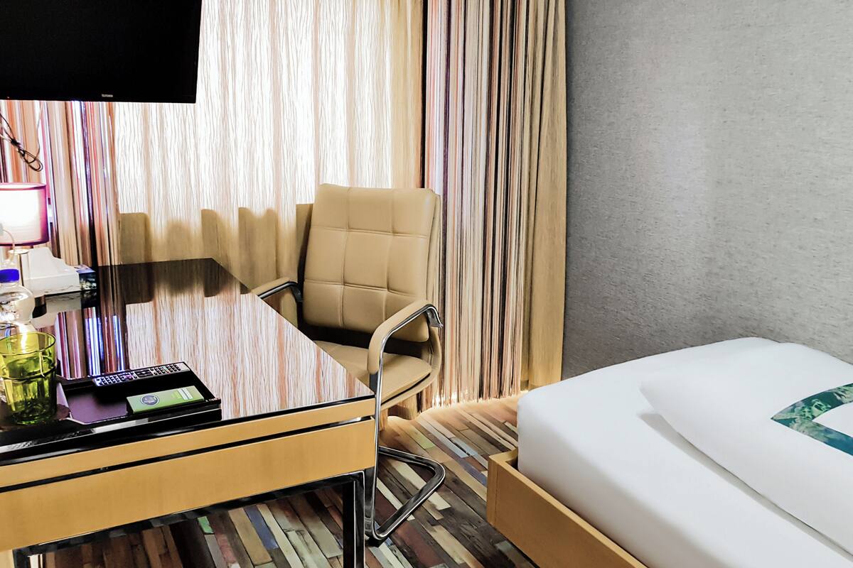 Una habitación de hotel con una cama, un escritorio con computadora, una silla y un televisor.