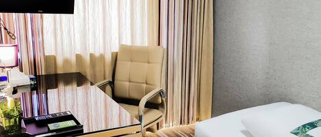 A hotel room with a bed, a desk with a computer, a chair, and a TV.