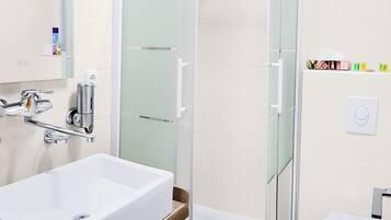 A modern bathroom with a large white sink, a glass shower enclosure, and a toilet.