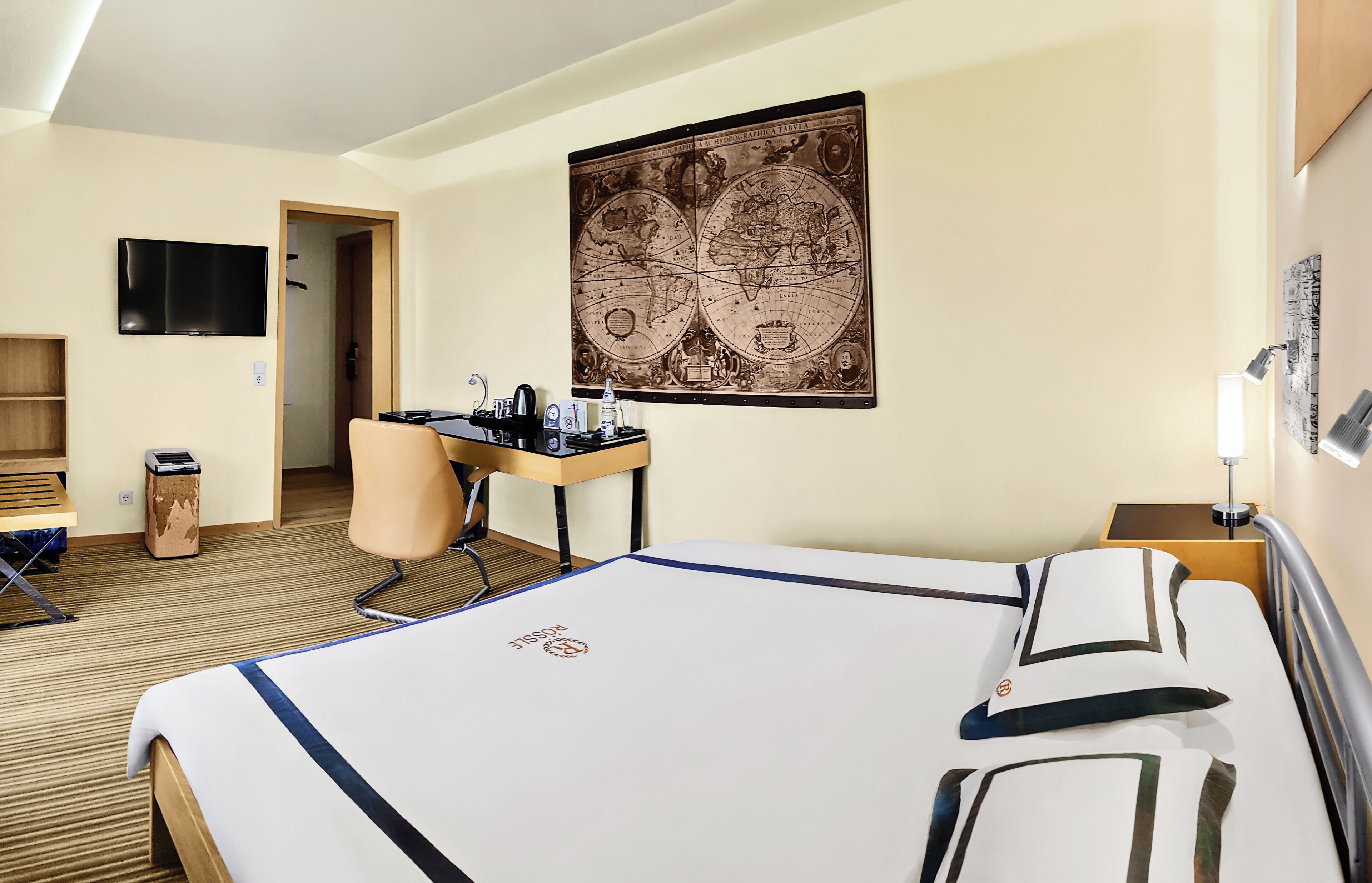 Habitación de hotel con cama, escritorio, silla y un gran mapa mural.