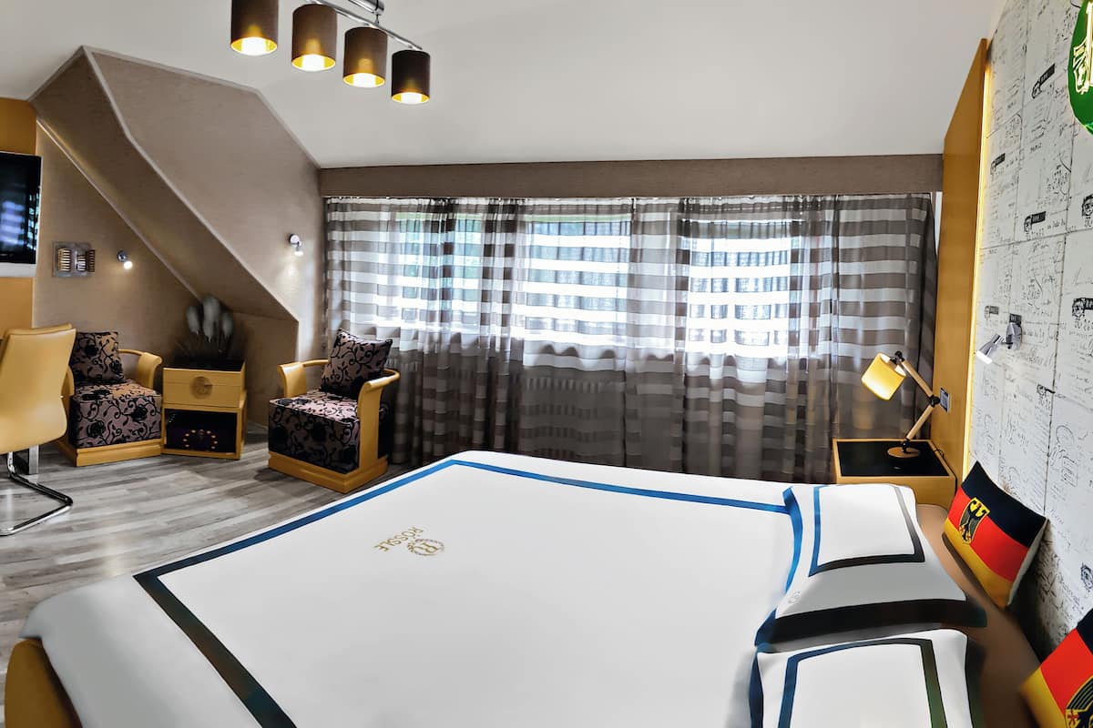 Una habitación de hotel con cama, escritorio, silla, televisor y ventana con cortinas.