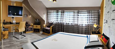 Una habitación de hotel con cama, escritorio, silla, televisor y ventana con cortinas.