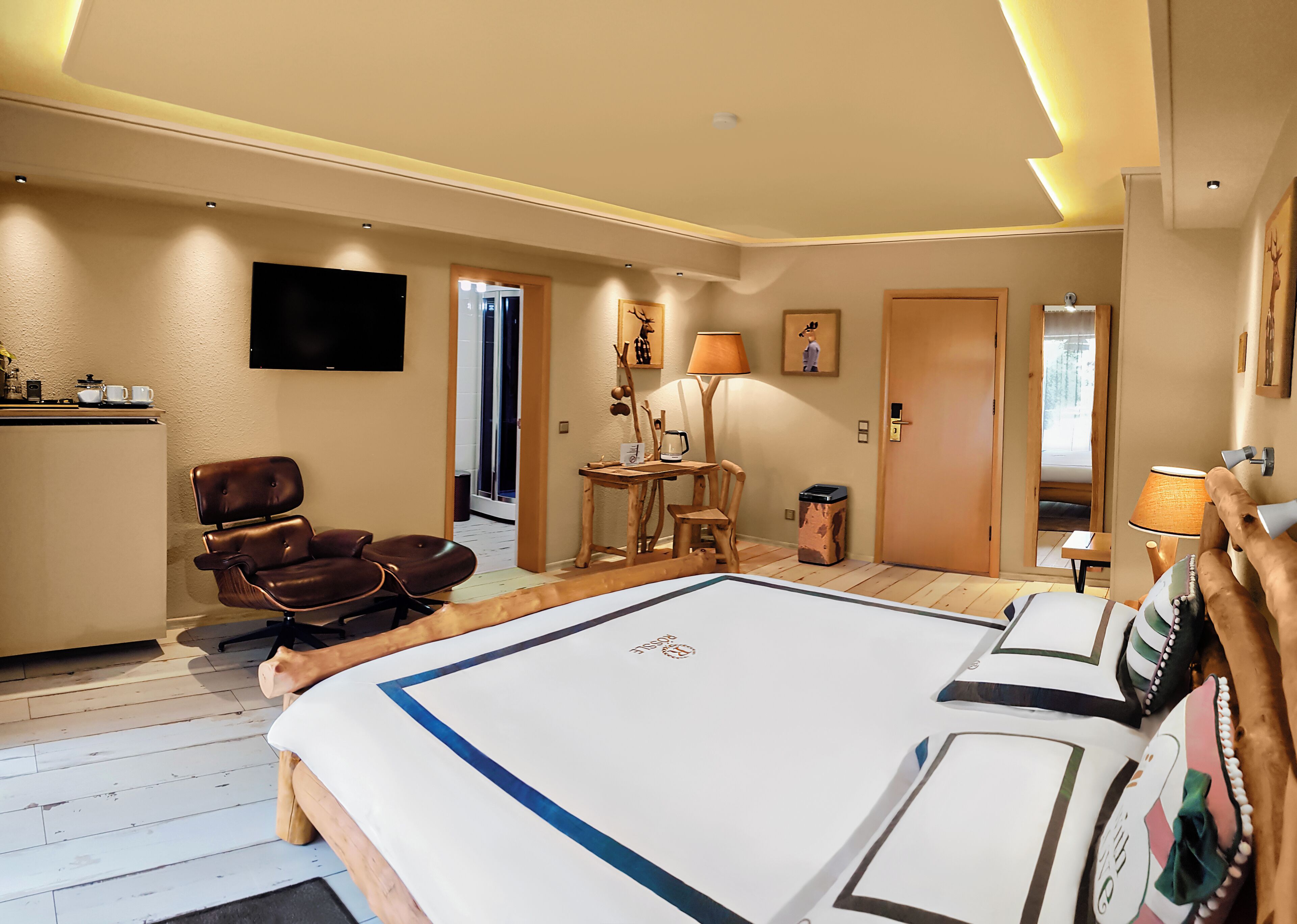 A hotel room with a large bed, a desk with a lamp, a chair, and a television on the wall.