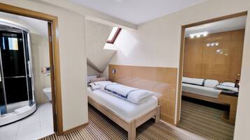 Una habitación de hotel moderna con cama, cabecero de madera, tragaluz pequeño y baño con inodoro y ducha.